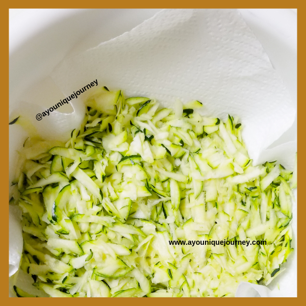 Grated Zucchini in a bowl with the paper towel absorbing the extra liquid.