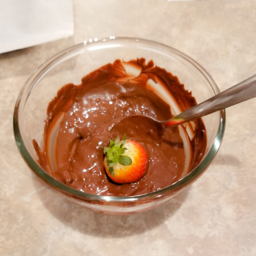 Dipping a strawberry in the melted dark chocolate.