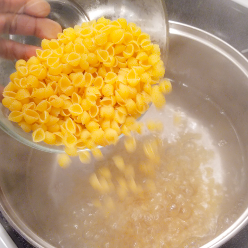 Pouring the mini shell pasta as directed on the package.
