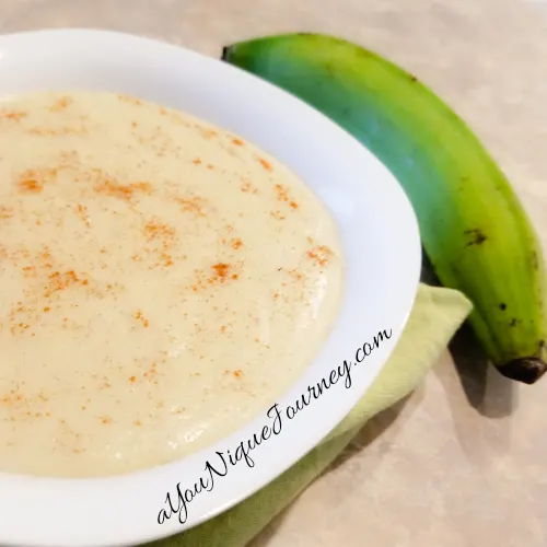 Plantain Porridge in a white bowl with a green plantain beside it.