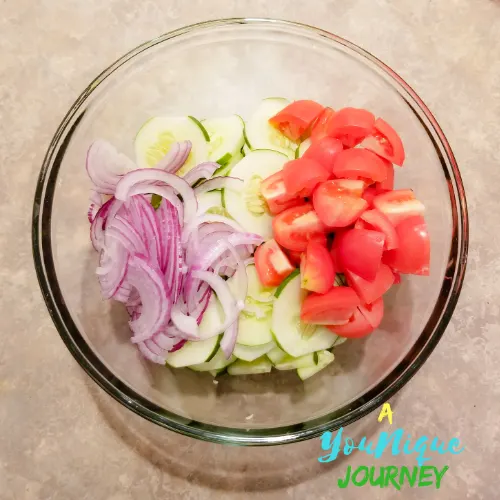 The slices cucumber, tomato and red onion in a large bowl.