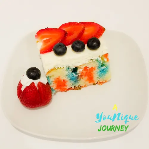 A piece of the red white and blue poke cake with a decorated strawberry with whipped cream and a blueberry on top.