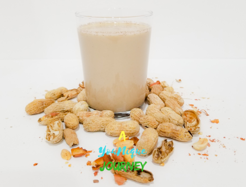 A glass of Peanut Punch with peanuts in shells around it.