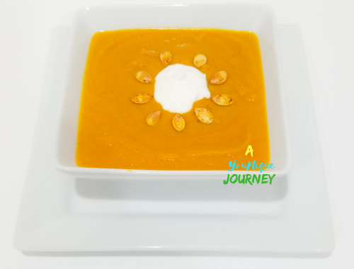 Pumpkin Soup with roasted pumpkin seeds and a dollop of sour cream on top in a white square bowl.