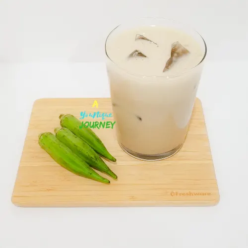 A glass of Okra Punch on a cutting board with 3 okras.