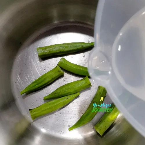 Adding water to the okras in a pot to boil.
