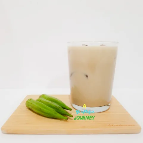 A glass of Okra Punch with 3 okras on a cutting board.