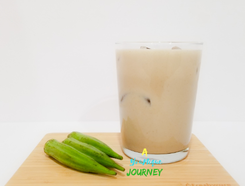 A glass of Okra Punch with 3 okras on a cutting board.