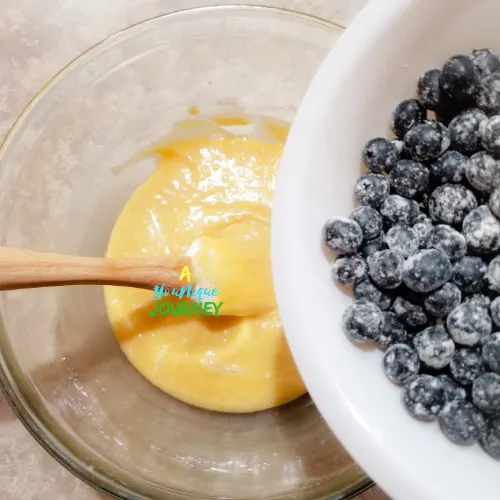Adding the coated blueberries to the mixture.