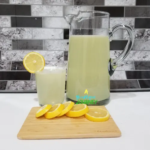 Lemonade in a pitcher and glass with lemon slices on a cutting board.