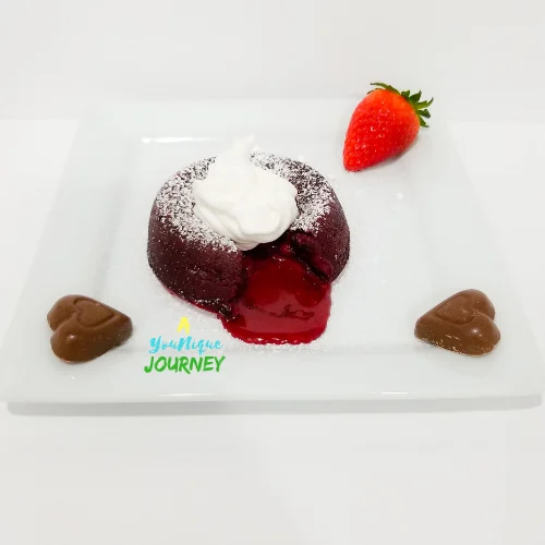 Red Velvet Molten Lava Cake on a serving plate with two heart shaped milk chocolate and a strawberry.