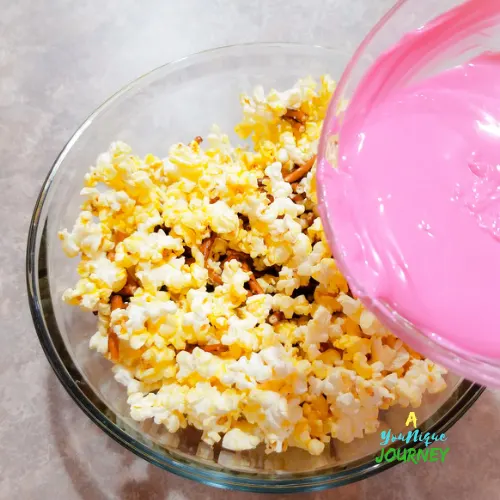 Pouring the melted candy melts wafers over the popcorn and broken pretzels.