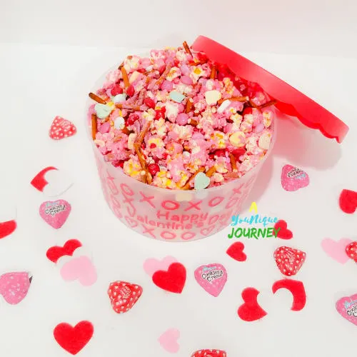 A bowl of Valentine's Day Popcorn Mix with heart shaped chocolates around it.