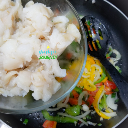 Adding the soaked saltfish to the sautéed vegetables and herbs.