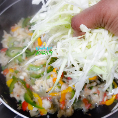 Adding the thinly sliced Cabbage to the Saltfish mixture.