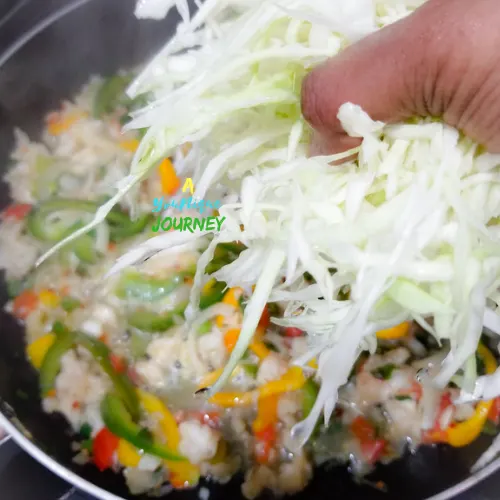Adding the thinly sliced Cabbage to the Saltfish mixture.