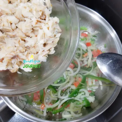 Adding the boiled saltfish to the sautéed vegetables and herbs. 