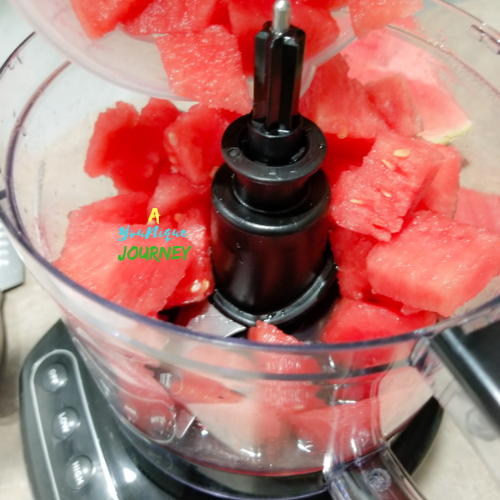 Adding chunks of watermelon to a food processor.