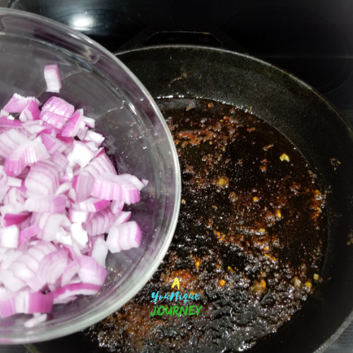 Adding the red onion to the cast iron skillet to make the One Pot Jerk Chicken with Rice and Peas.