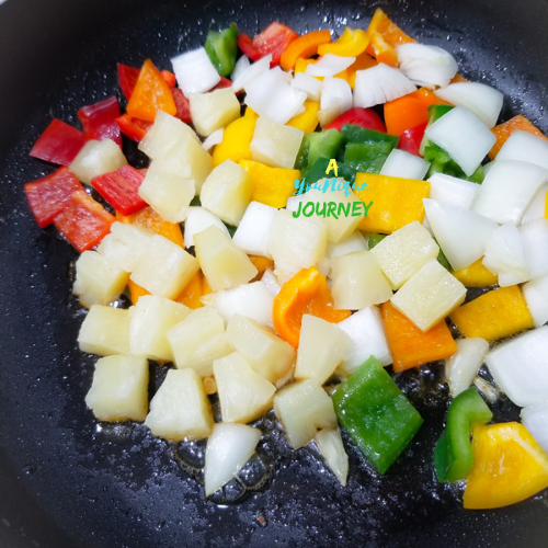 Vegetables and pineapple chunks saute to make sweet and sour chicken.
